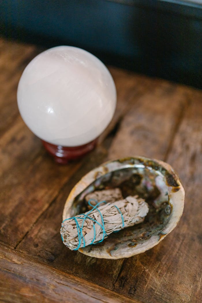 A crystal ball and sage bundle placed on a wooden table symbolize spirituality and cleansing.